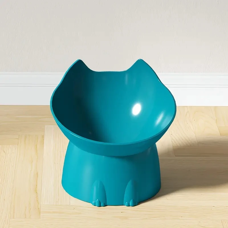 Gamelle surélevée bleu canard en forme de tête de chat à oreilles, sur un parquet clair devant un mur beige