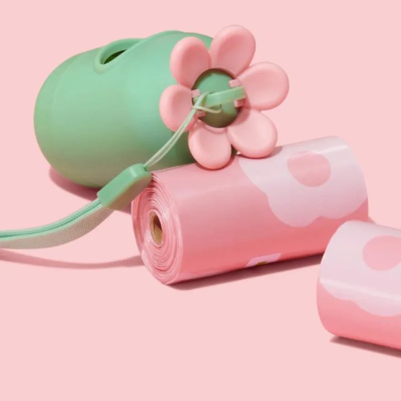 Distributeur de sacs à déjections vert à fleur rose, à côté de rouleaux de sacs roses