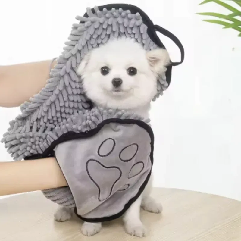 Chien blanc enveloppé dans une serviette de séchage chenille grise, maintenue à deux mains
