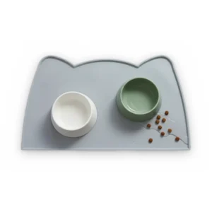 Set de table en silicone gris-bleu en forme de tête de chat avec une gamelle blanche et une gamelle verte, vu de dessus